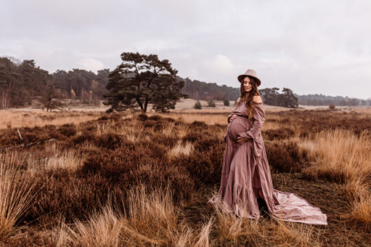 zwangerschap zwangerschapsshoot zwanger loonse en drunense duinen vrouw met hoed en paarse jurk heeft buik vast